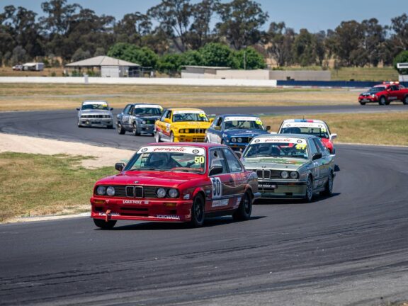Group of classic BMW race cars competing on a track during a motorsport event.