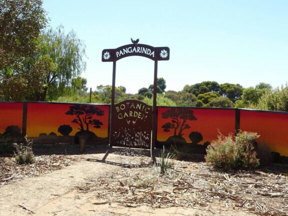 Entrance sign to Pangarinda Botanic Garden with painted sunset mural in the background.