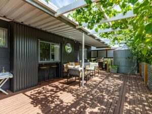 Shaded outdoor deck with seating area beside a modern corrugated cabin.