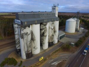 Large grain silos painted with black-and-white mural art beside a highway.
