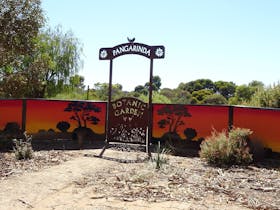 Entrance sign to Pangarinda Botanic Garden with painted sunset mural in the background.