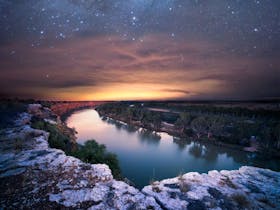Sun setting over the a river with a clear night sky full of stars