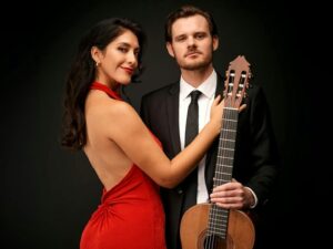 Woman in red dress posing with a man in black suit and guitar in hand