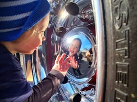 Little kid seeing reflection in the hub cap of a truck wheel