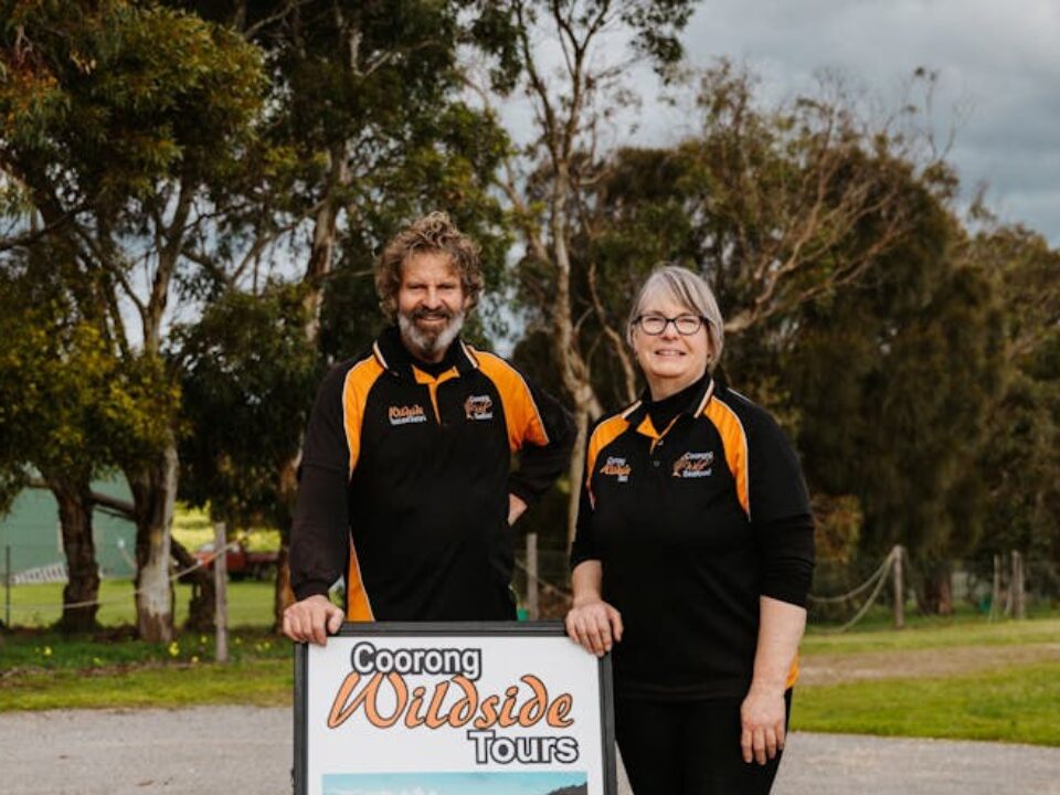 Man and woman standing behind an A-frame signage that says Coorong Wildside Tours