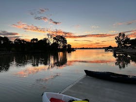 beautiful sunset reflects off the river with trees on the banks and a dock with two canoes