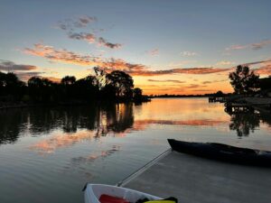 beautiful sunset reflects off the river with trees on the banks and a dock with two canoes